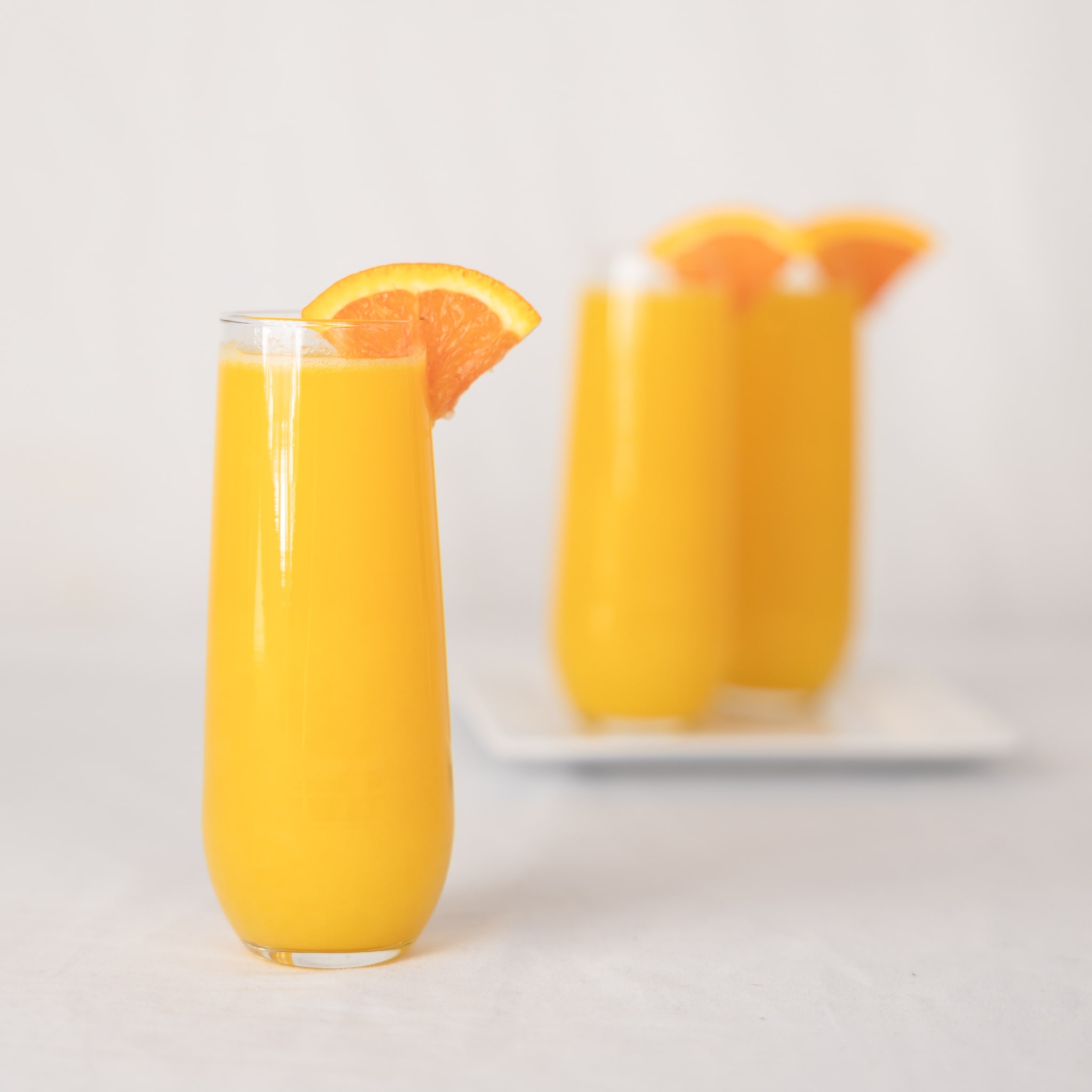 Tall glass of bright orange juice garnished with an orange slice, additional glasses blurred in the background